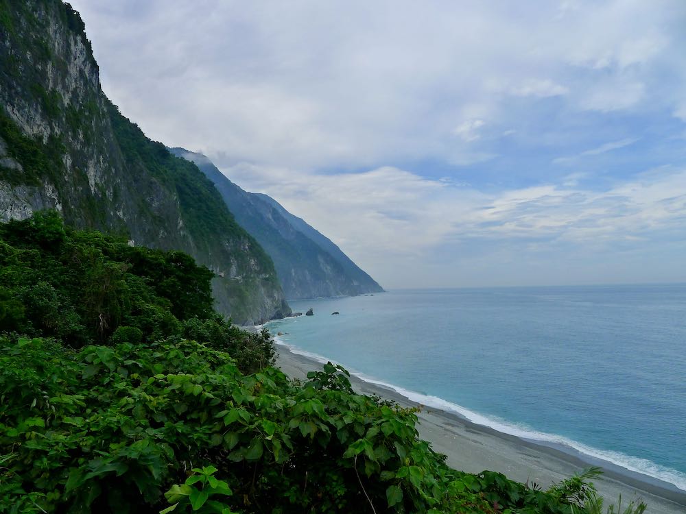 Steep cliffs covered in green foliage, beach, and bright blue ocean at Qingshui lookout