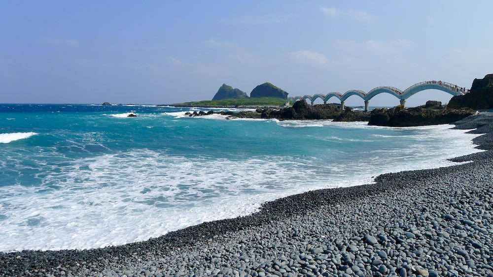 Bright blue ocean, pebble beach, and Sanxiantai eight-arch bridge leading to island