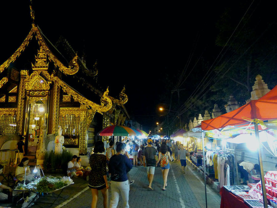 People walk by a temple and clothing stalls at the Sunday Walking Street market in Chiang Mai's Old City.