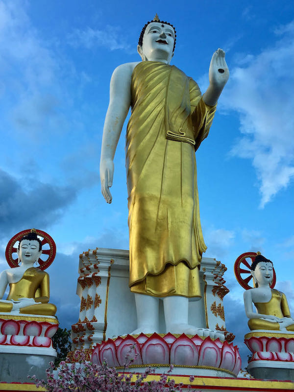 Golden standing Buddha in between two seated Buddha statues at Wat Phrathat Doi Kham.