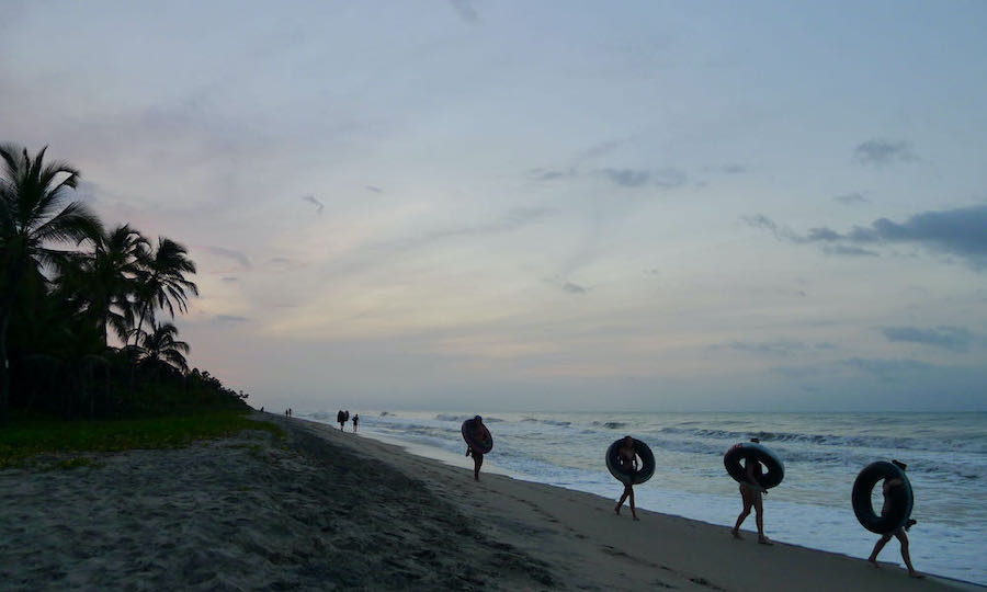 Travelers carrying inner tubes walk back to Palomino Beach in Colombia at sunset.