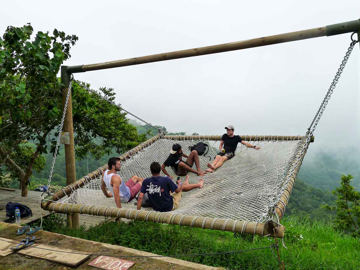 Four backpackers swing in a giant hammock at a hostel overlooking the misty mountains of Minca.