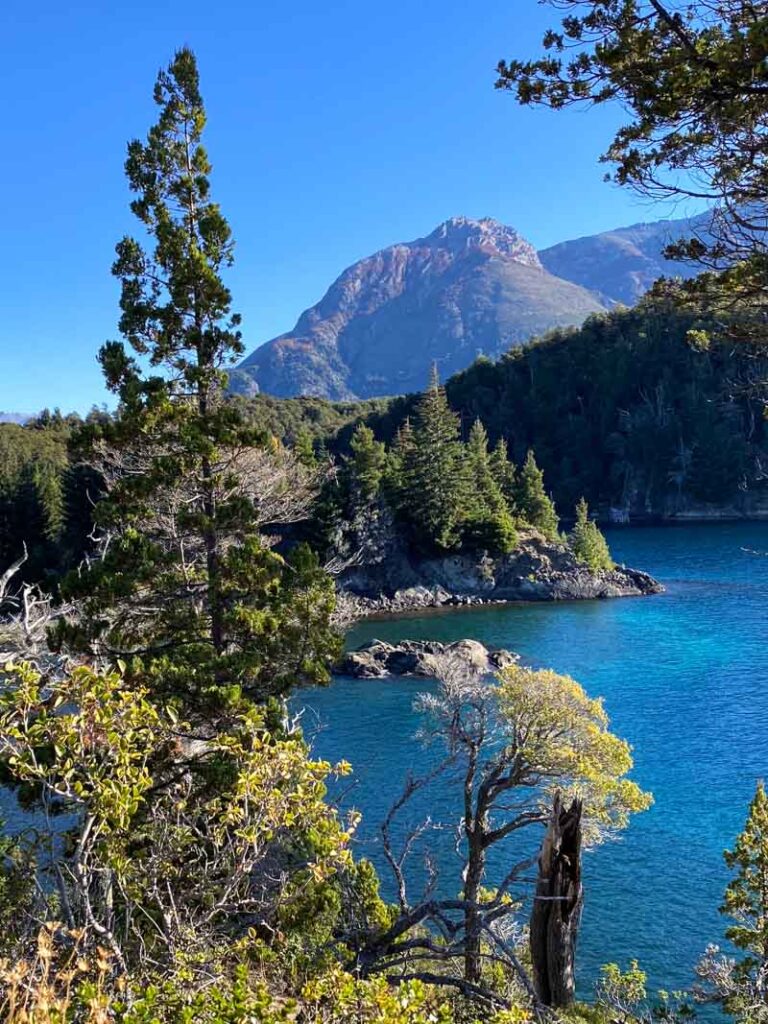 Different shades of blue in Tacul Bay surrounded by trees and mountains in the background.