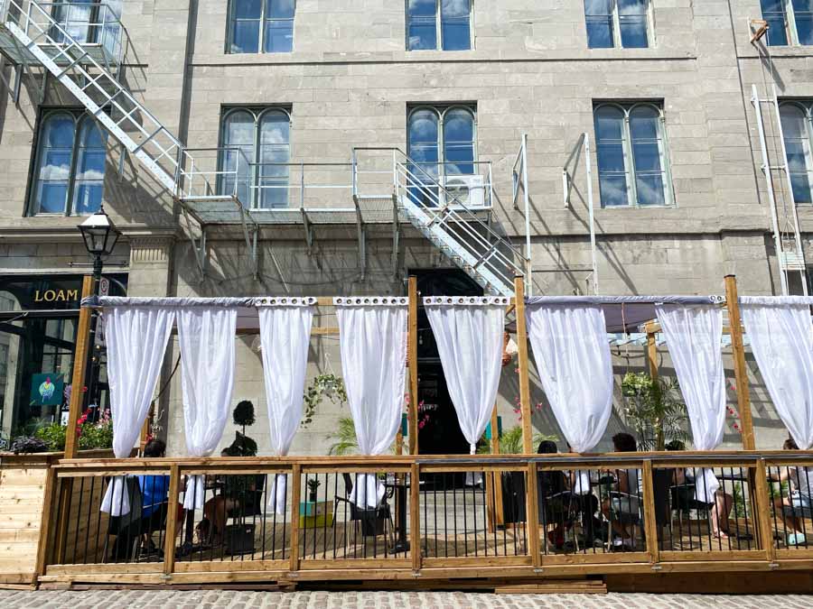 An outdoor terrace with white curtains on a cobblestone street in early summer, the best time of year to visit Montreal.