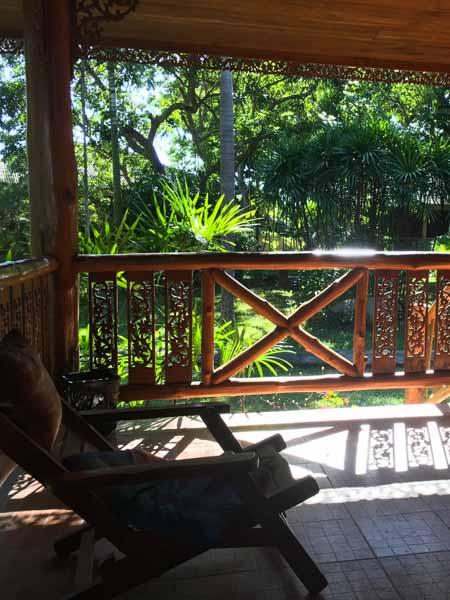 A chair on the porch of a classic northern Thai wooden bungalow surrounded by green plants in Chiang Dao.