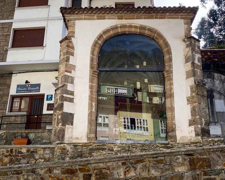 Colorful buildings reflected in the window of the Capilla del Humilladero, with a crucifix visible through the glass.
