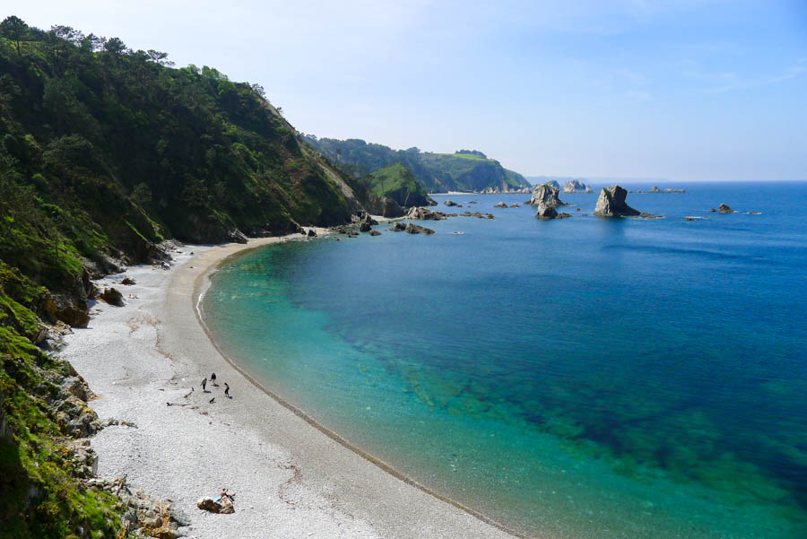 Three people walk with their dog on the pebble beach of Playa del Silencio in Asturias, northern Spain.