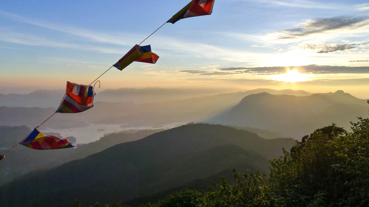 Sun rising behind mountains and prayer flags on Adam's Peak.