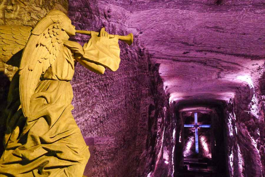 A stone angel statue and large cross under purple lighting in the underground Salt Cathedral in Zipaquirá, an easy day trip from Bogotá.