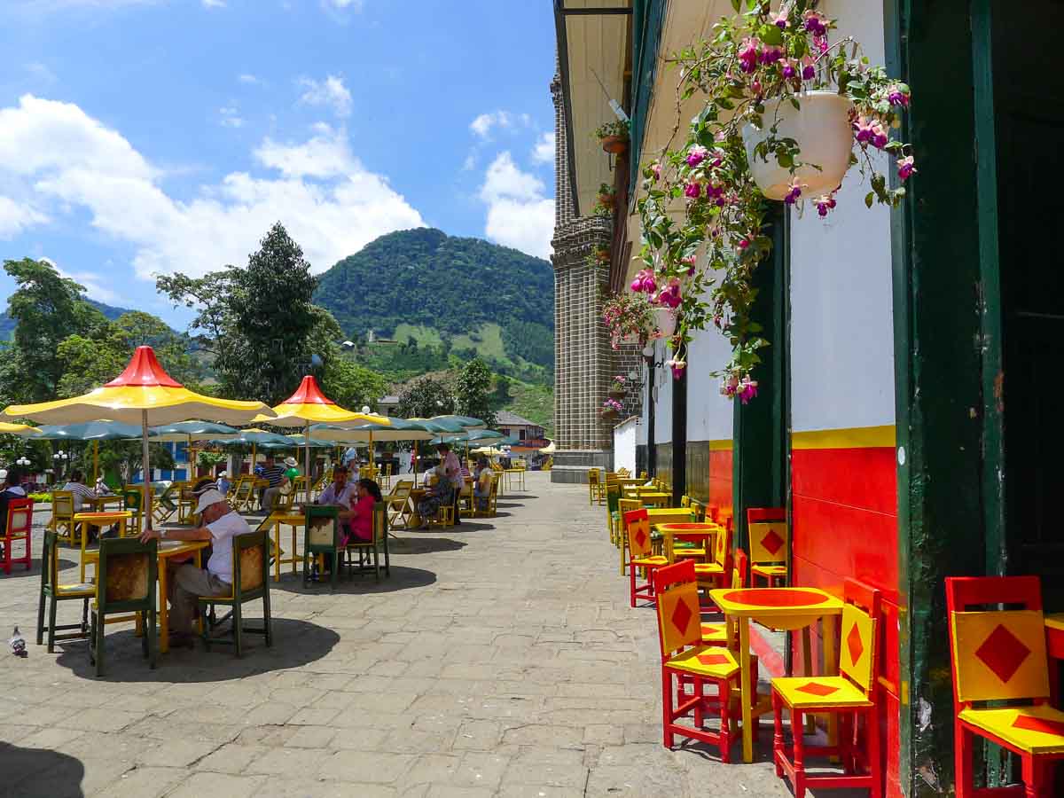 Brightly colored tables and chairs with sun umbrellas in the main square of Jardín, Colombia.