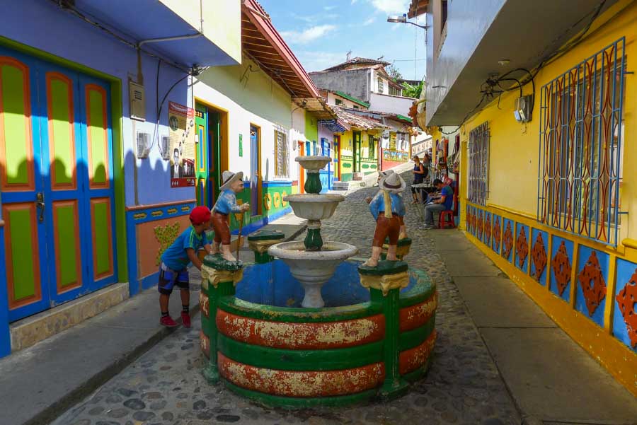 Multicolored buildings along a cobblestone street with a round fountain in Guatapé, a great day trip from Medellín.