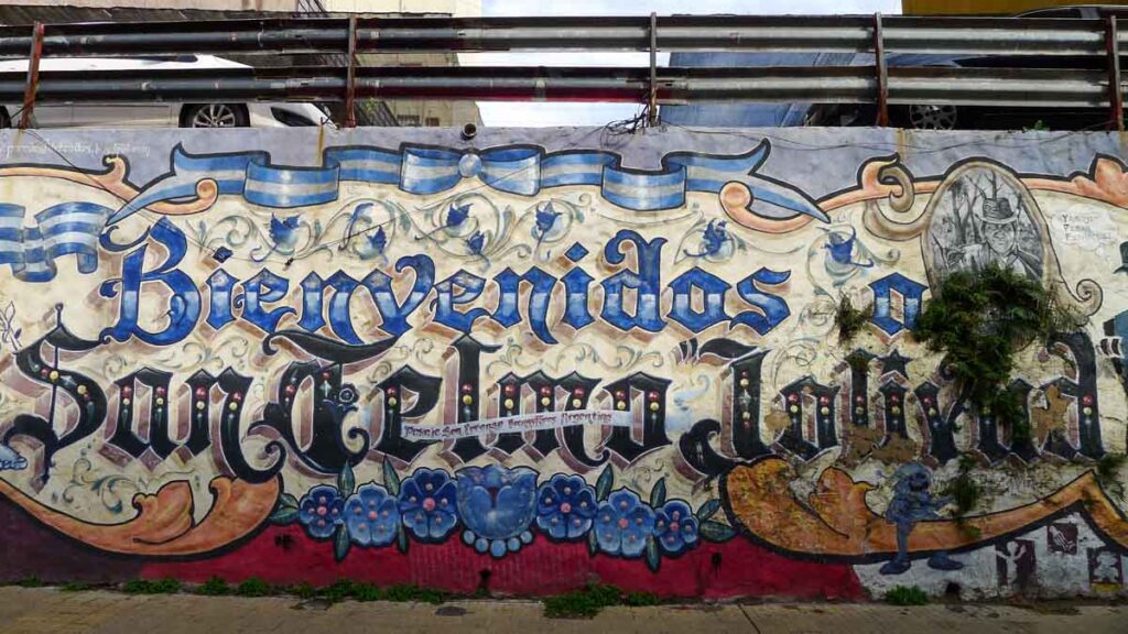 Mural that reads "Bienvenidos a San Telmo Jolivud" with fileteado porteño styling.
