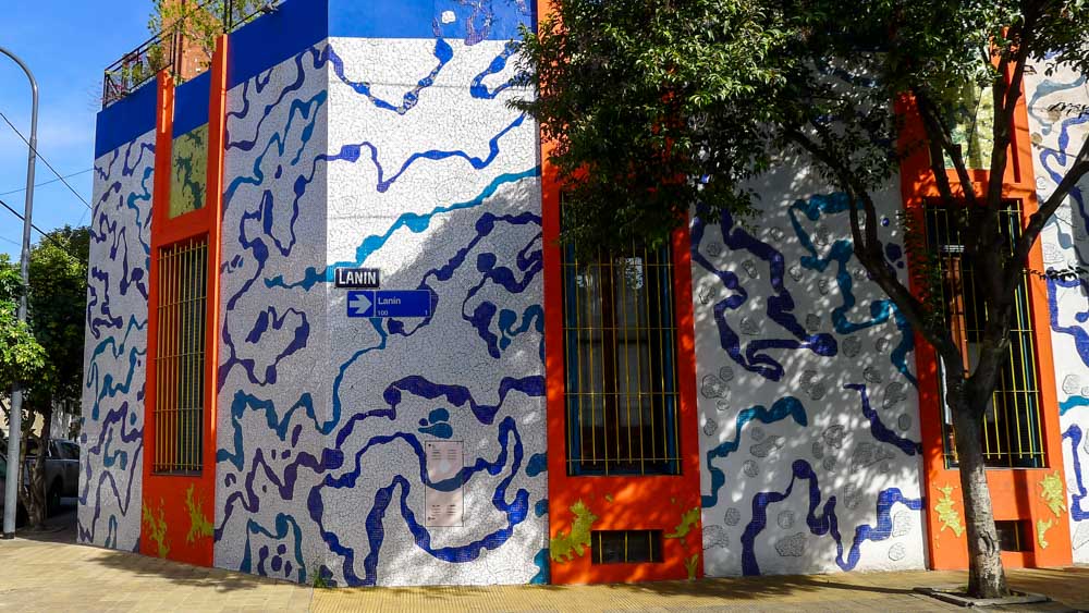 Corner building with orange panels and a blue and white mosaic with the "Lanín" street sign visible on the wall.