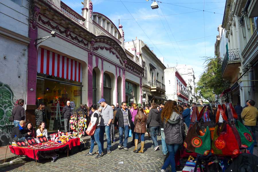 Crowds browse leather bags and other crafts along cobblestone Defensa Street at the San Telmo Fair on a Sunday afternoon.
