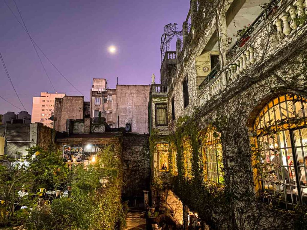 Evening on the ivy-covered terrace of Atis Bar in San Telmo. The moon is visible above and there is warm light coming from the arches of the old convent building.