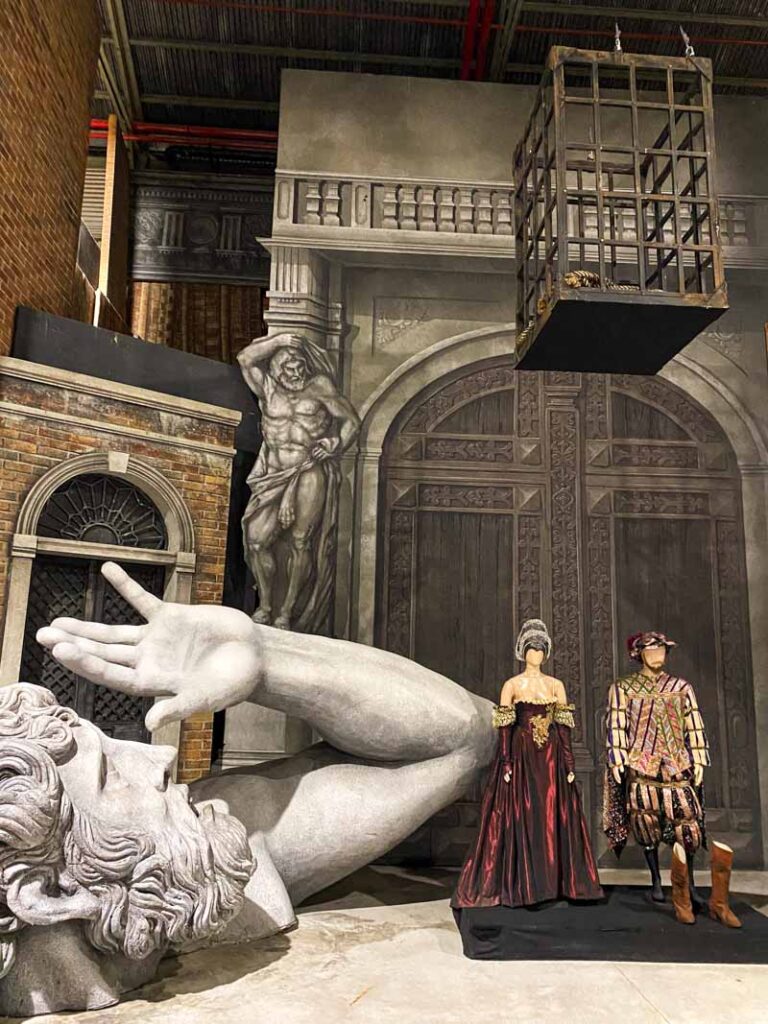 The set of Rigoletto opera, including a large sculpture, a hanging cage, and period costumes displayed at Colón Fábrica.