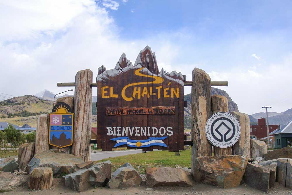 The welcome sign you see when you arrive in El Chaltén, displaying an outline of Fitz Roy mountain and the town's nickname, the "National Capital of Trekking."