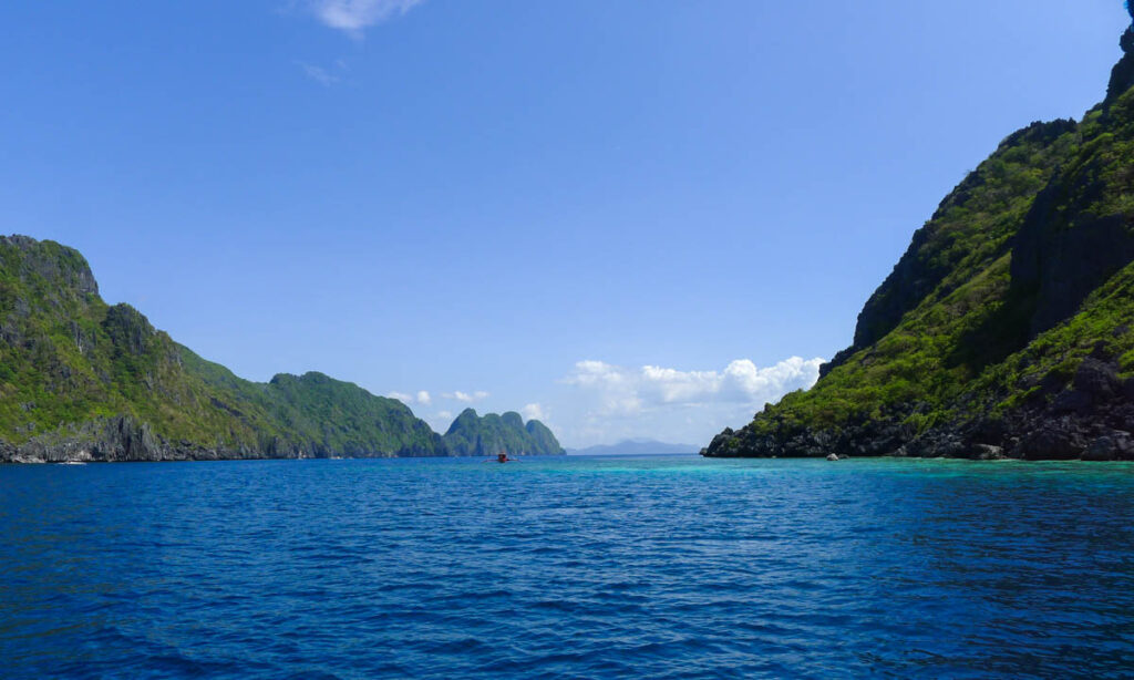 A small boat in blue and turquoise water surrounded by limestone karsts near Matinloc Island.