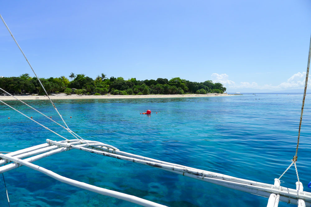 The crystal clear water of Balicasag Island, with coral gardens just below the surface and snorkelers visible in the distance.