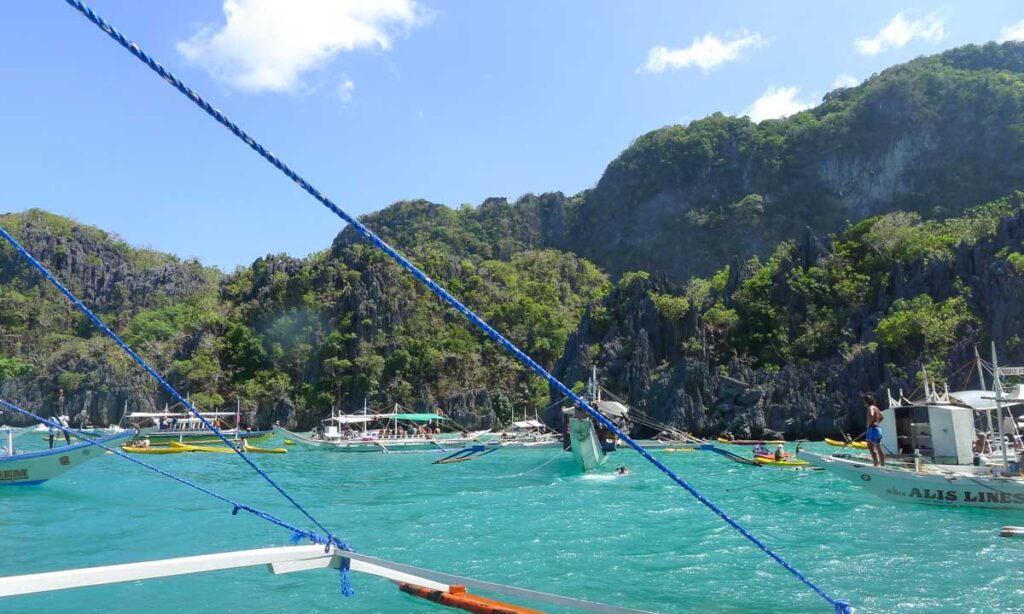 Many island-hopping tour outrigger boats and sea kayaks crammed into a small bay in El Nido, Philippines.