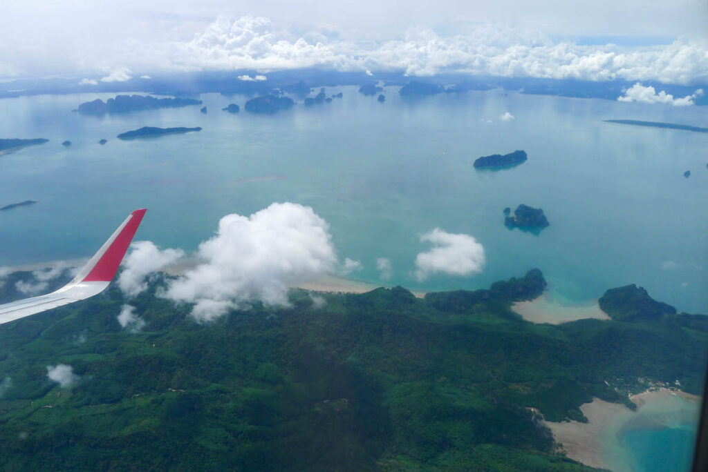 Beaches, turquoise water, and limestone islands viewed from the window of a plane landing at Phuket airport.