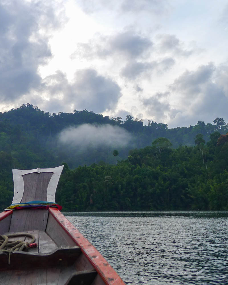 Front of a longtail boat on Cheow Lan Lake with misty jungle in the background.