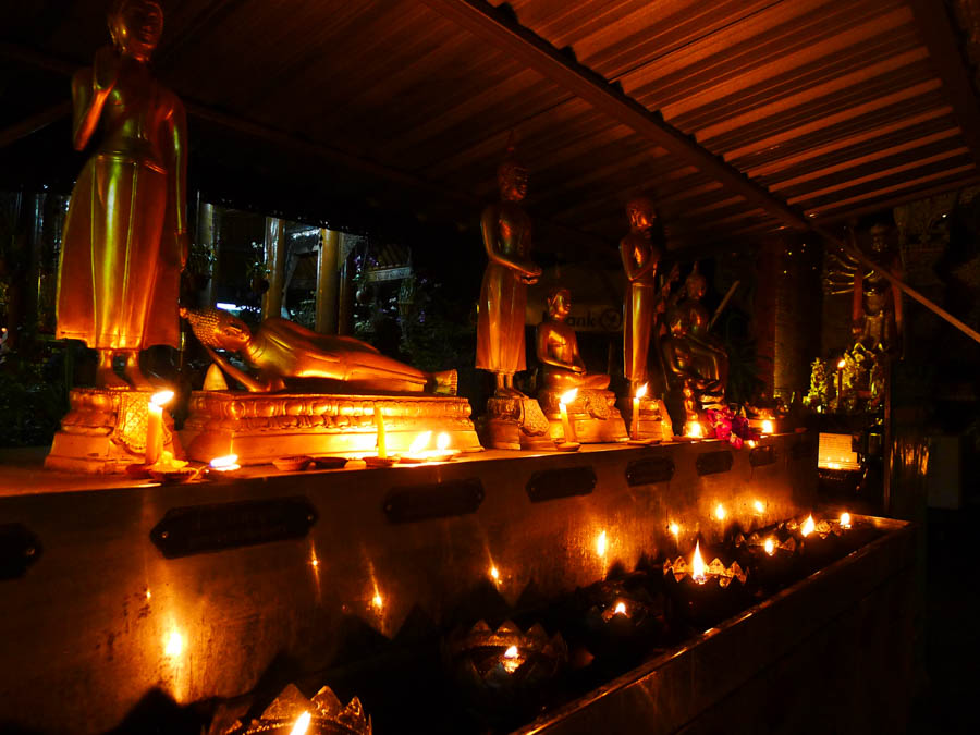 Small Buddha statues and floating candles at a Chiang Mai temple at night.
