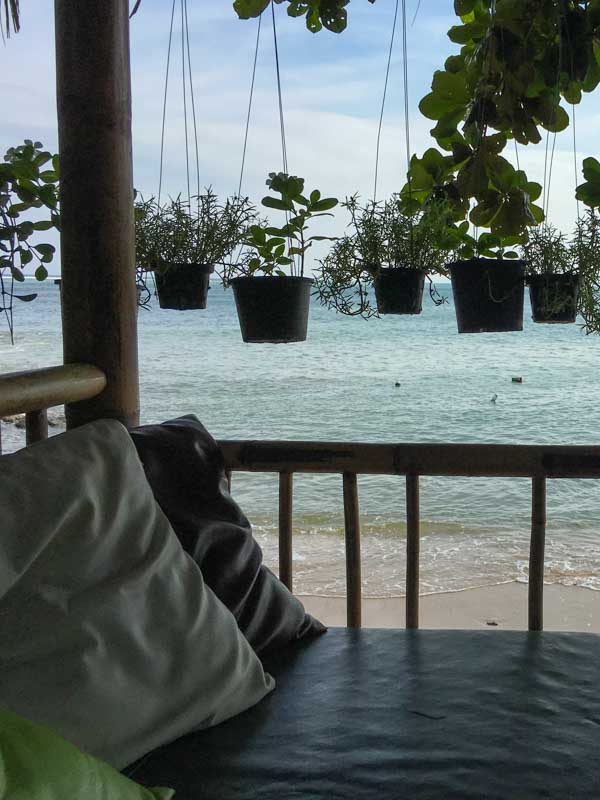 Looking out at the ocean from a small beach structure with cushions, pillows, and plants on Koh Samui.