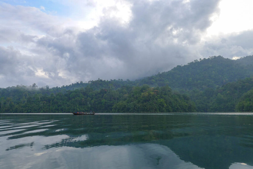 A longtail boat takes visitors on an evening wildlife safari on Cheow Lan Lake. The clouds and jungle are reflected in the water.