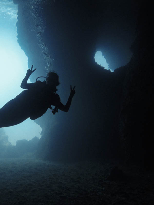 A scuba diver (me) posing for a photo making peace signs in the dark cavern of Koh Haa's Cathedral dive site.