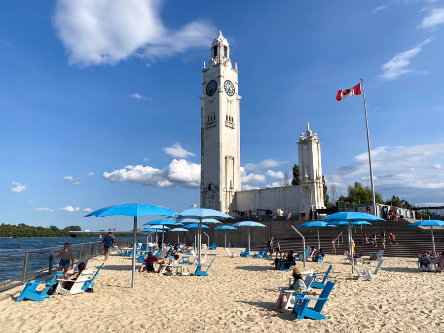 Blue umbrellas and chairs in the sand at the Plage d'Horlage under the Clock Tower in Montreal's Old Port.