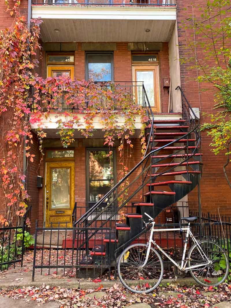 A classic Montreal street scene with a bicycle parked in front of a twisty outside staircase draped with fall leaves.