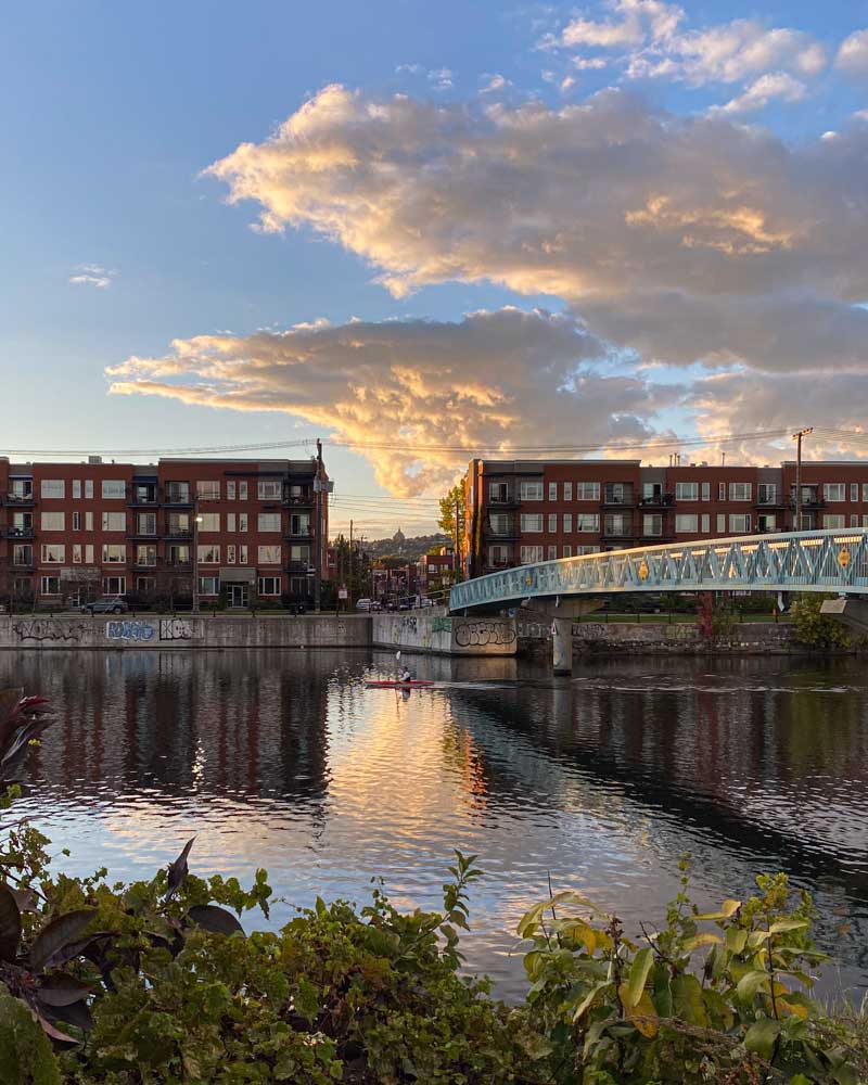A kayaker passing under a bridge on the Lachine Canal in Saint-Henri. Saint Joseph's Oratory is visible in the distance.