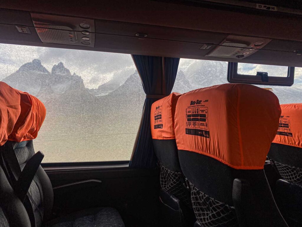 The snowy Paine Massif viewed from a bus window, with orange Bus Sur covers on the seats in the foreground.