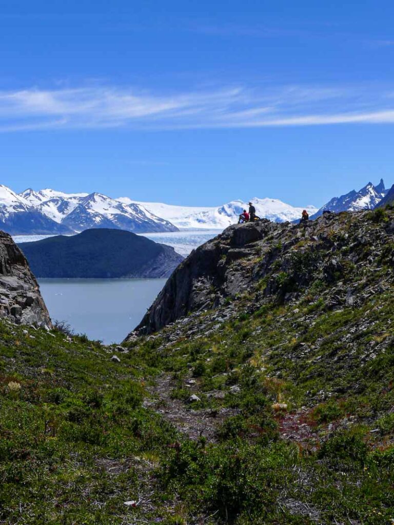Hikers take a break at Lago Grey viewpoint with glacier and mountains in distance.