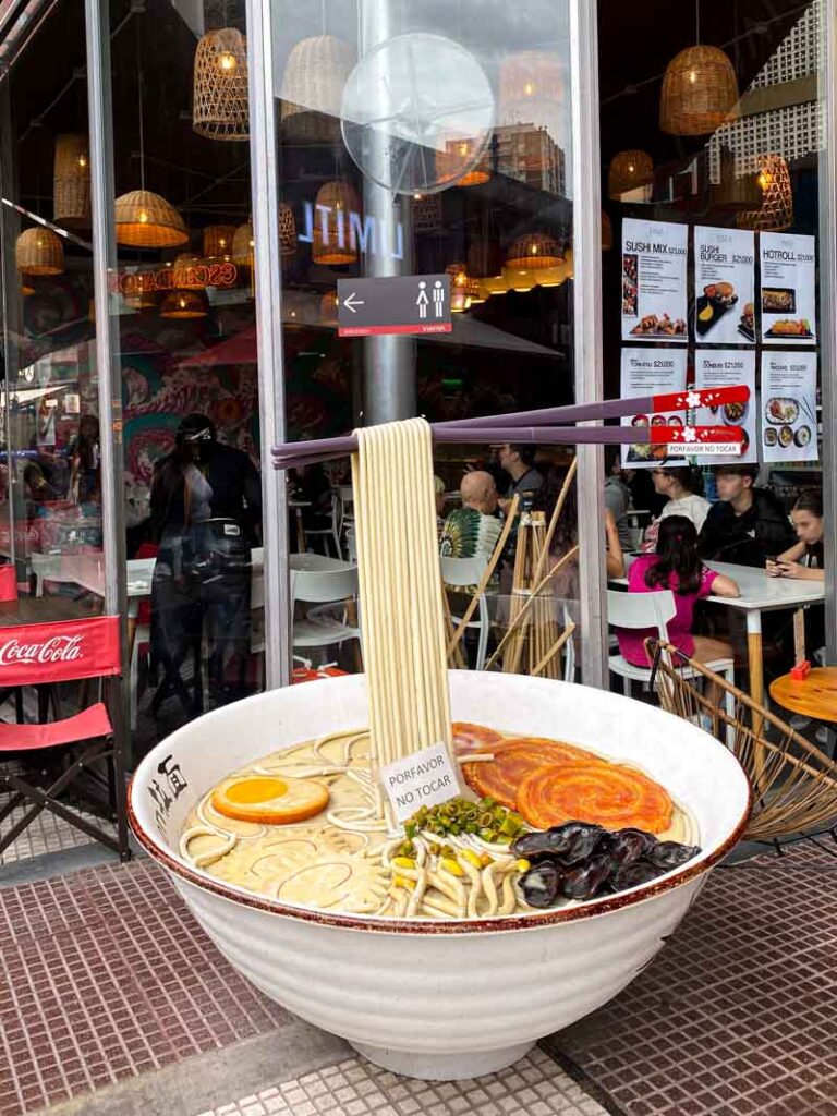 Large sculpture of a bowl of ramen noodles and chopsticks outside a restaurant on the Via Viva in Belgrano.