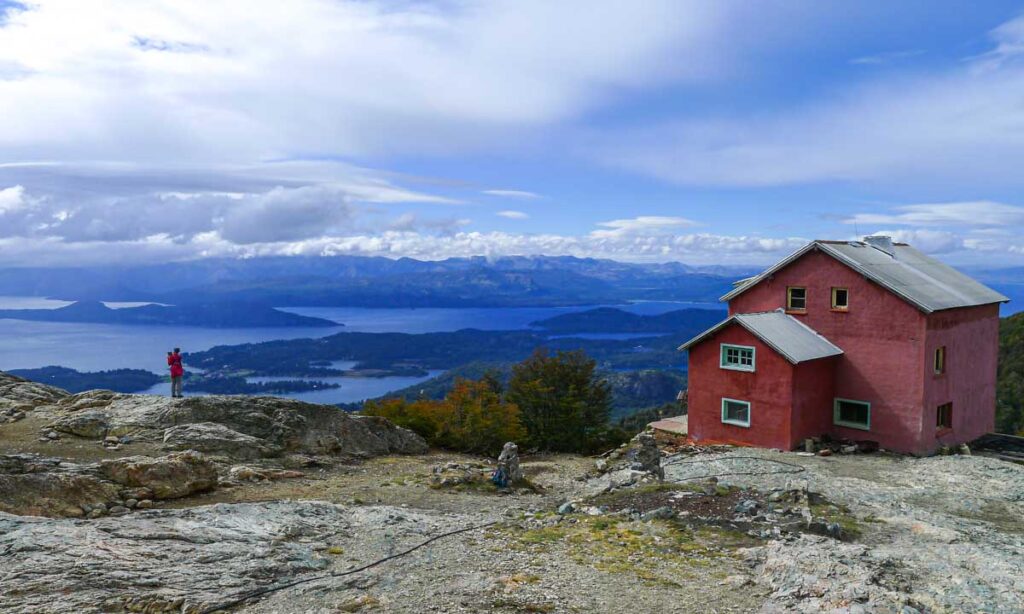 A hiker taking photos at Refugio López, with panoramic views of Bariloche's lakes and mountains.