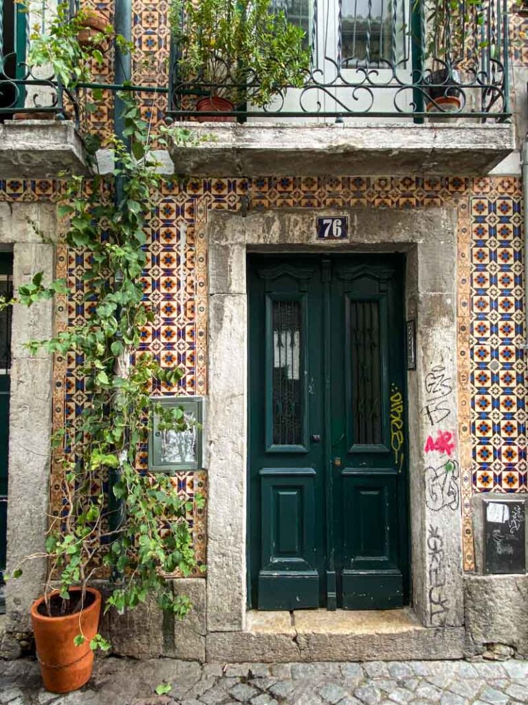 A typical Portuguese door surrounded by colorful azulejo tiles and green plants.
